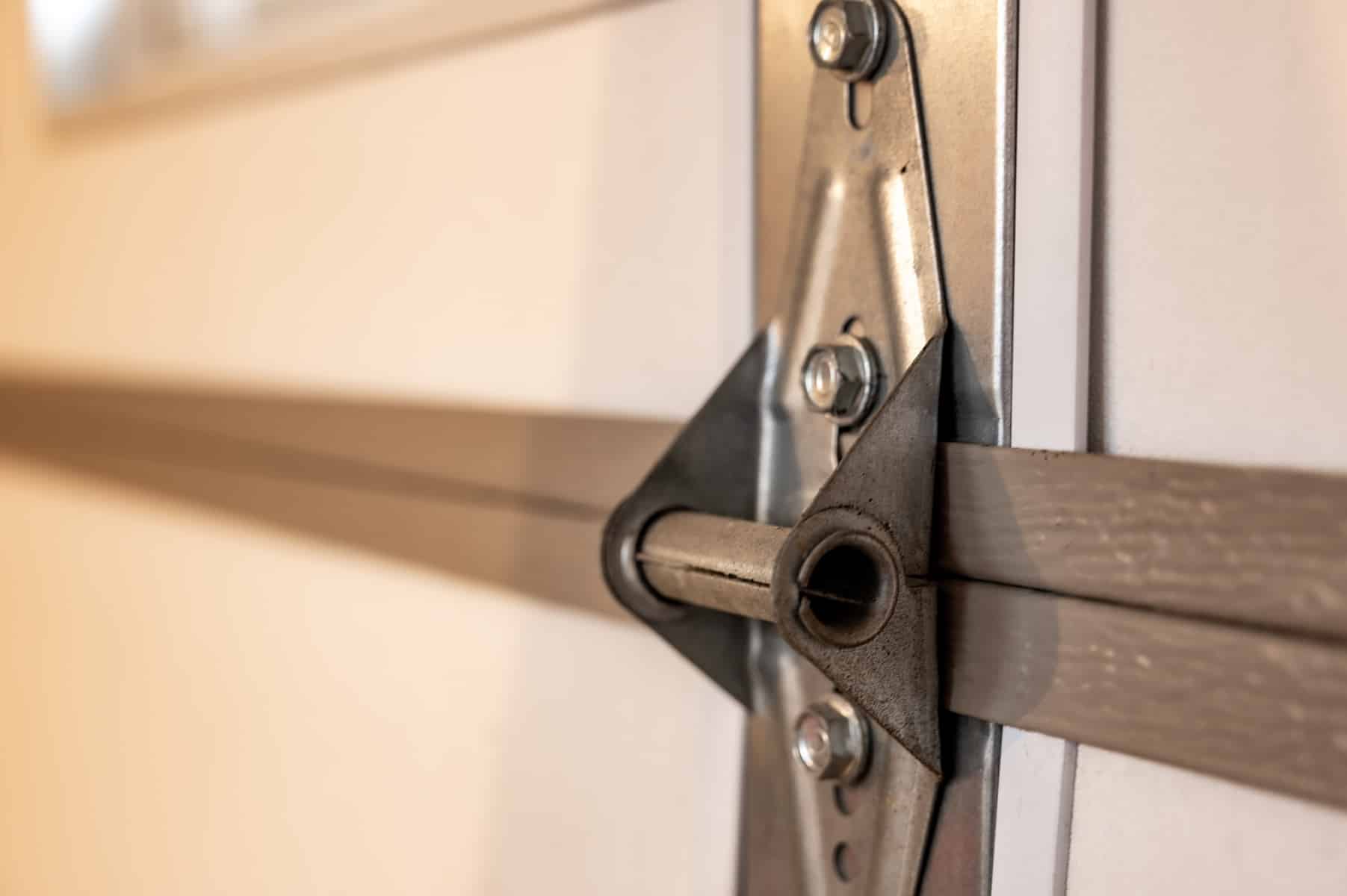 Close-up of a metal hinge and bracket on a white garage door, showing the connection of the door panels and the supporting hardware in detail.