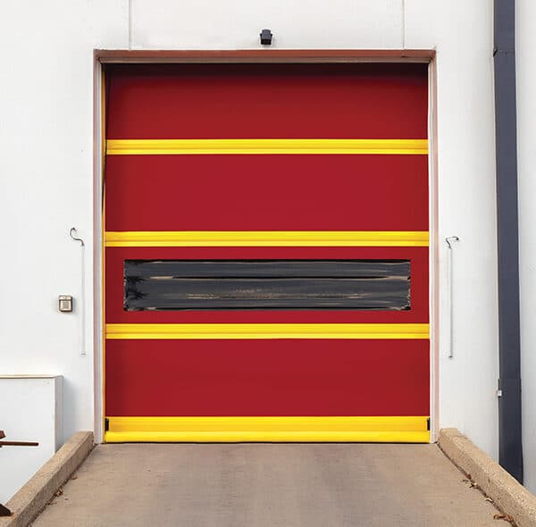 A red industrial garage door with yellow stripes and a central black window at a concrete loading dock outside a commercial building.