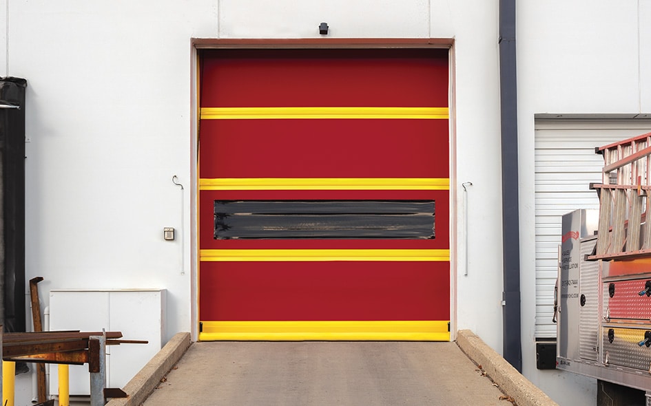 A red industrial garage door with yellow stripes and a central black window at a concrete loading dock outside a commercial building.