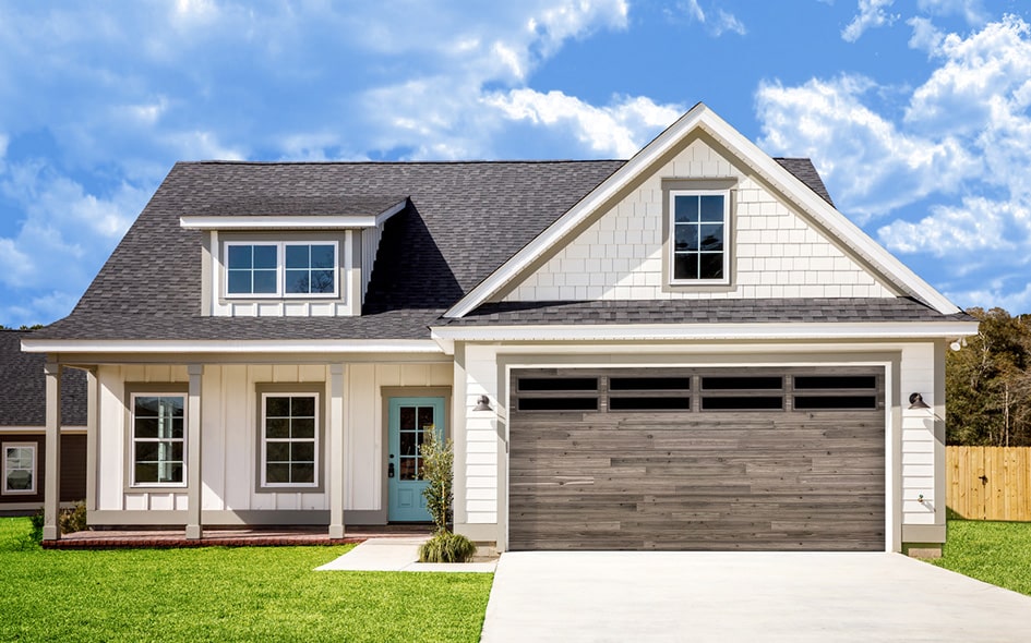 Modern suburban house with white siding, dark gray roof, large wooden garage door, and front porch under a bright blue sky.