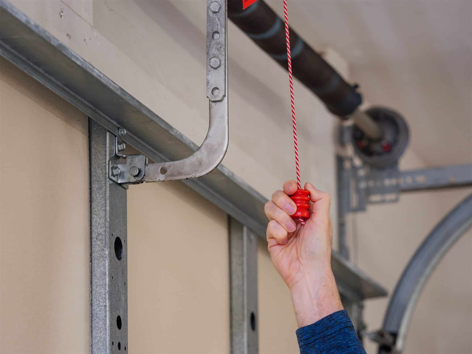 Man pulling manual safety release cord handle before performing maintenance on electric garage door opener